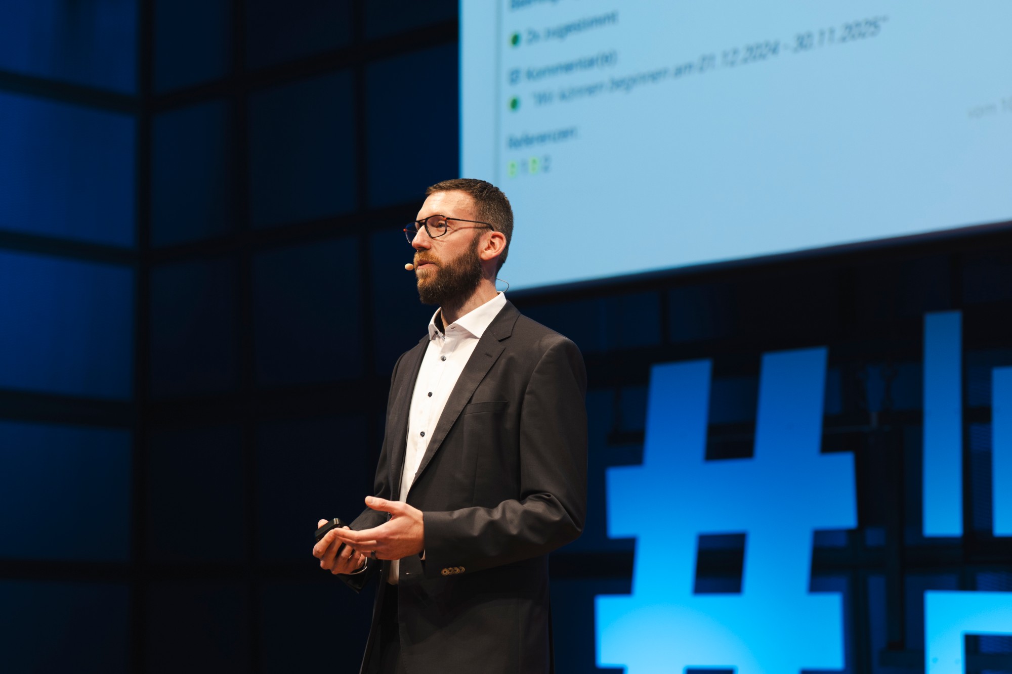 Benjamin Berger hält auf dem InnovationFestival Karlsruhe einen Vortrag auf der Bühne, im Hintergrund eine Folie mit Prüfergebnissen