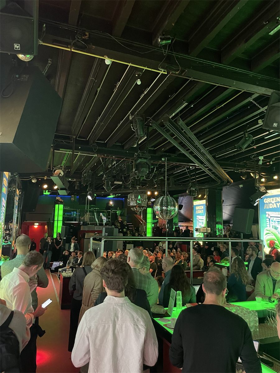 A full house at Green AI Day 2025 in Stuttgart: the audience in a venue lit in green, with Green AI Day banners at the sides